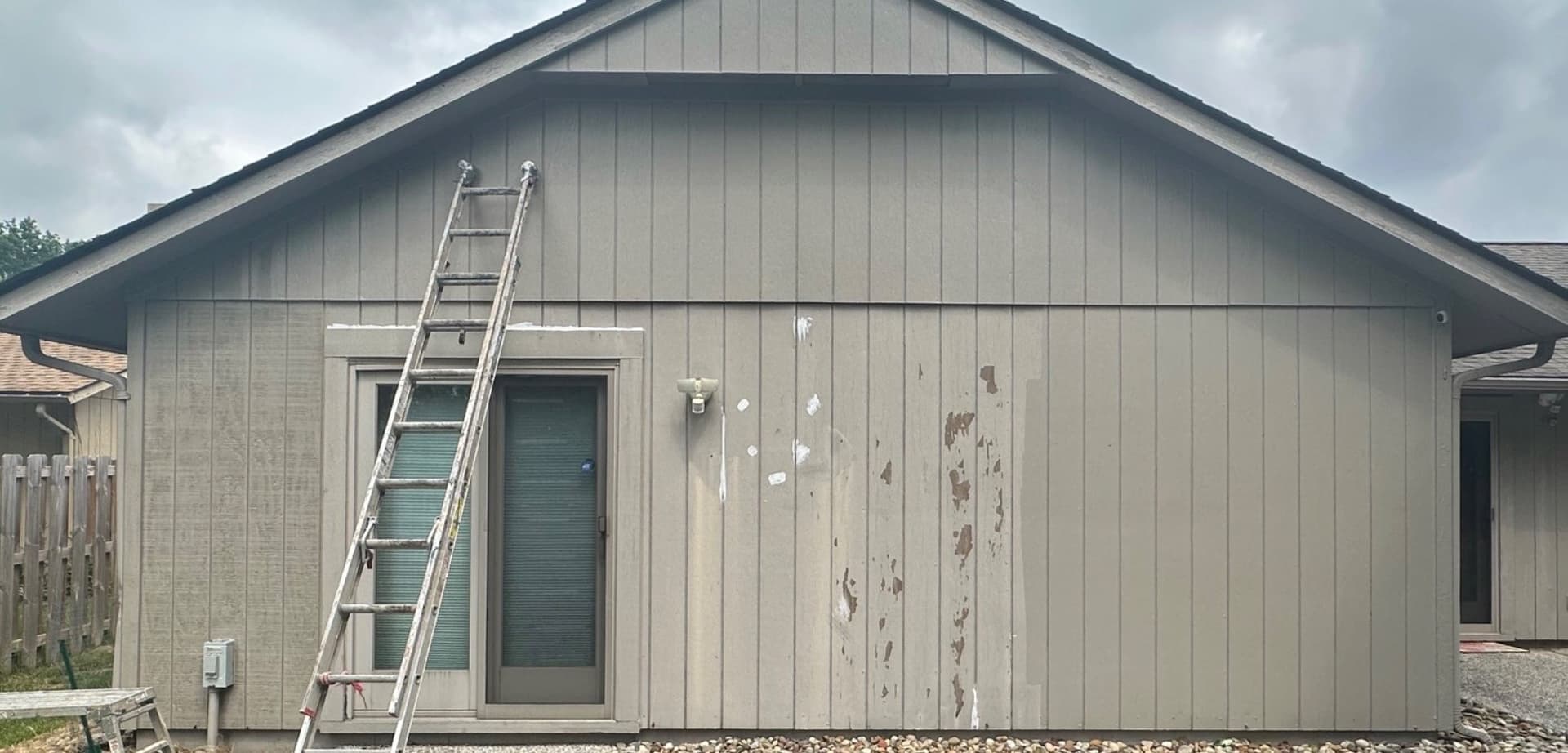 Gray garage siding with peeling patches and bare wood showing, before