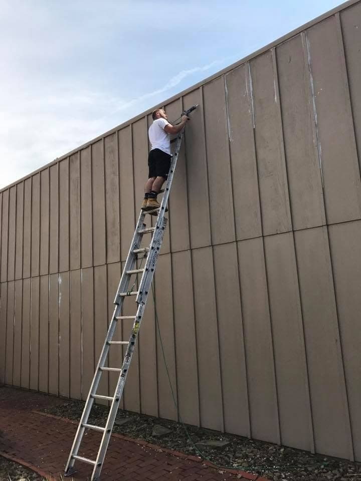 A Wildwood painter on a tall ladder brushing a high wall of vertical siding